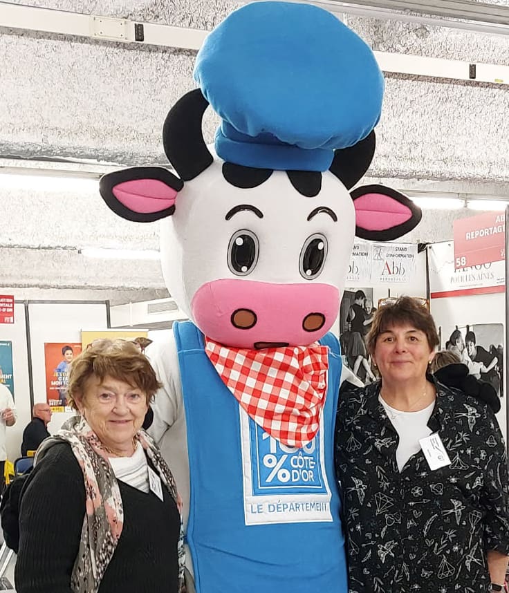 Photo Annick et Michèle avec la mascotte 100 % Côte d'Or qui est une magnifique vache avec une toque de cuisinier et un tablier bleus.